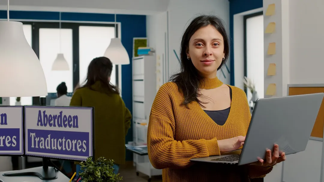 Profesional de la traducción con portátil en mano en oficina con logotipo visible de Aberdeen Traductores